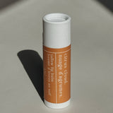 Genesis Tallow Lip balm with a white cap and brown label on a light gray background