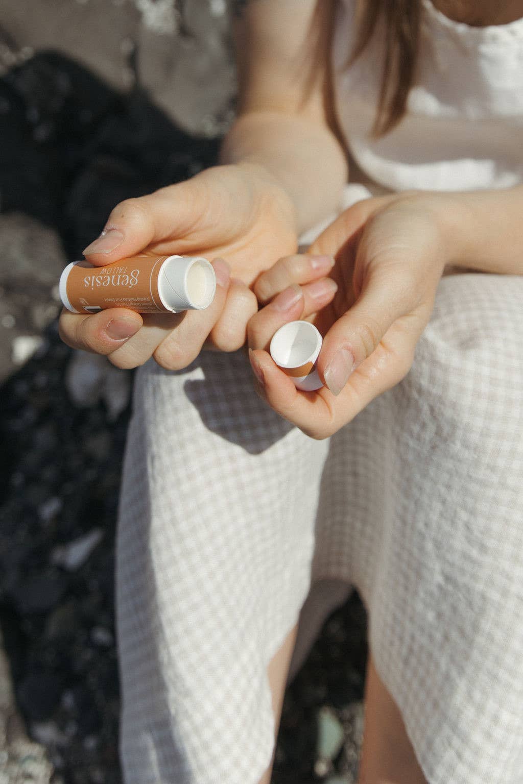 Genesis Tallow lip balm held by hands against a blurred background