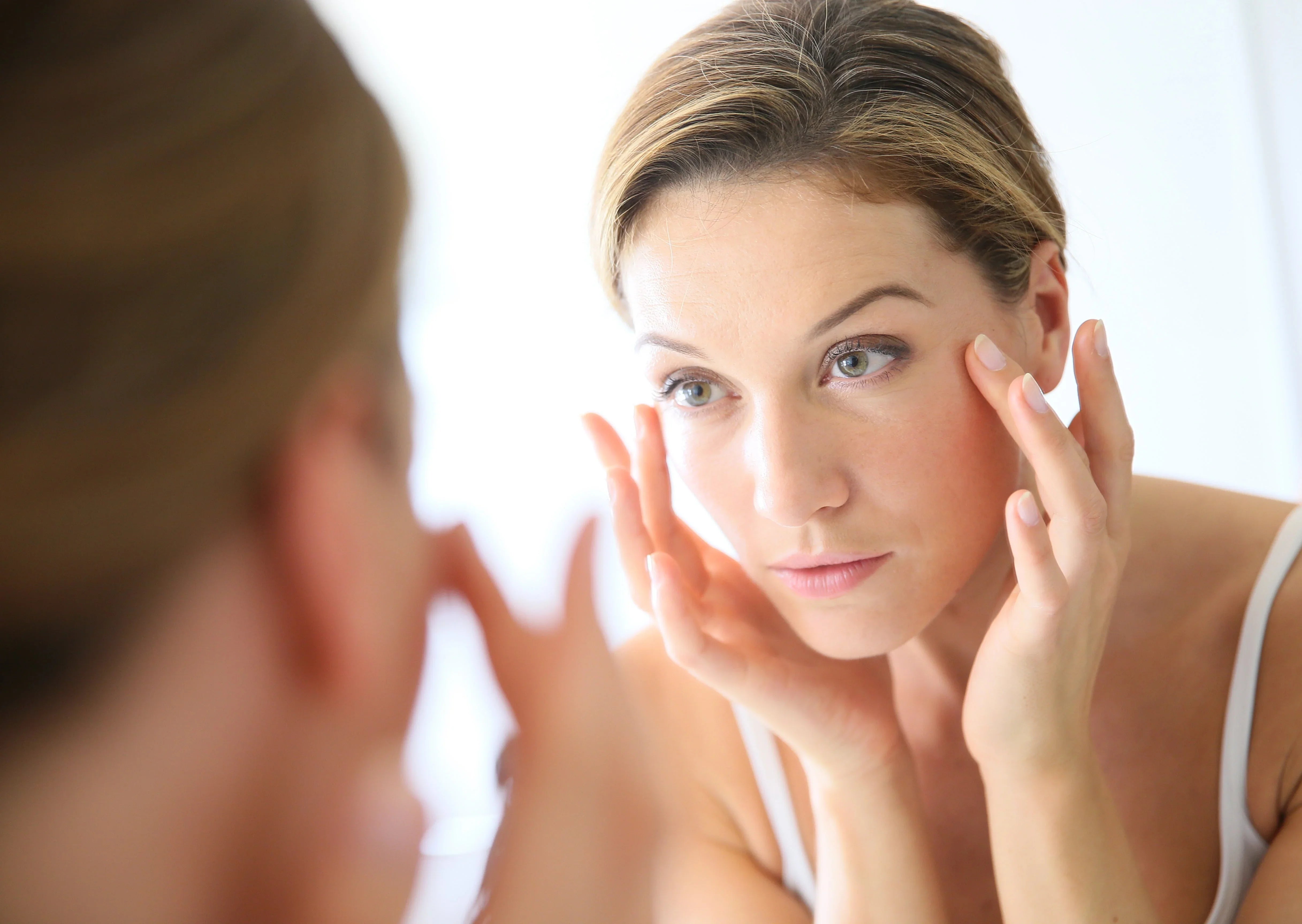 Woman applying eye cream in mirror