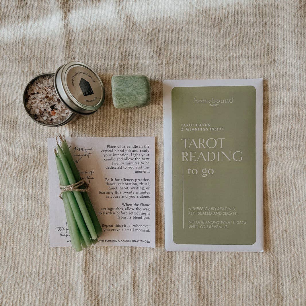 Tarot reading kit with tarot cards, candles, and a crystal on textured surface