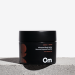 Black jar of Om Organics whipped body butter on a light gray surface with a white background