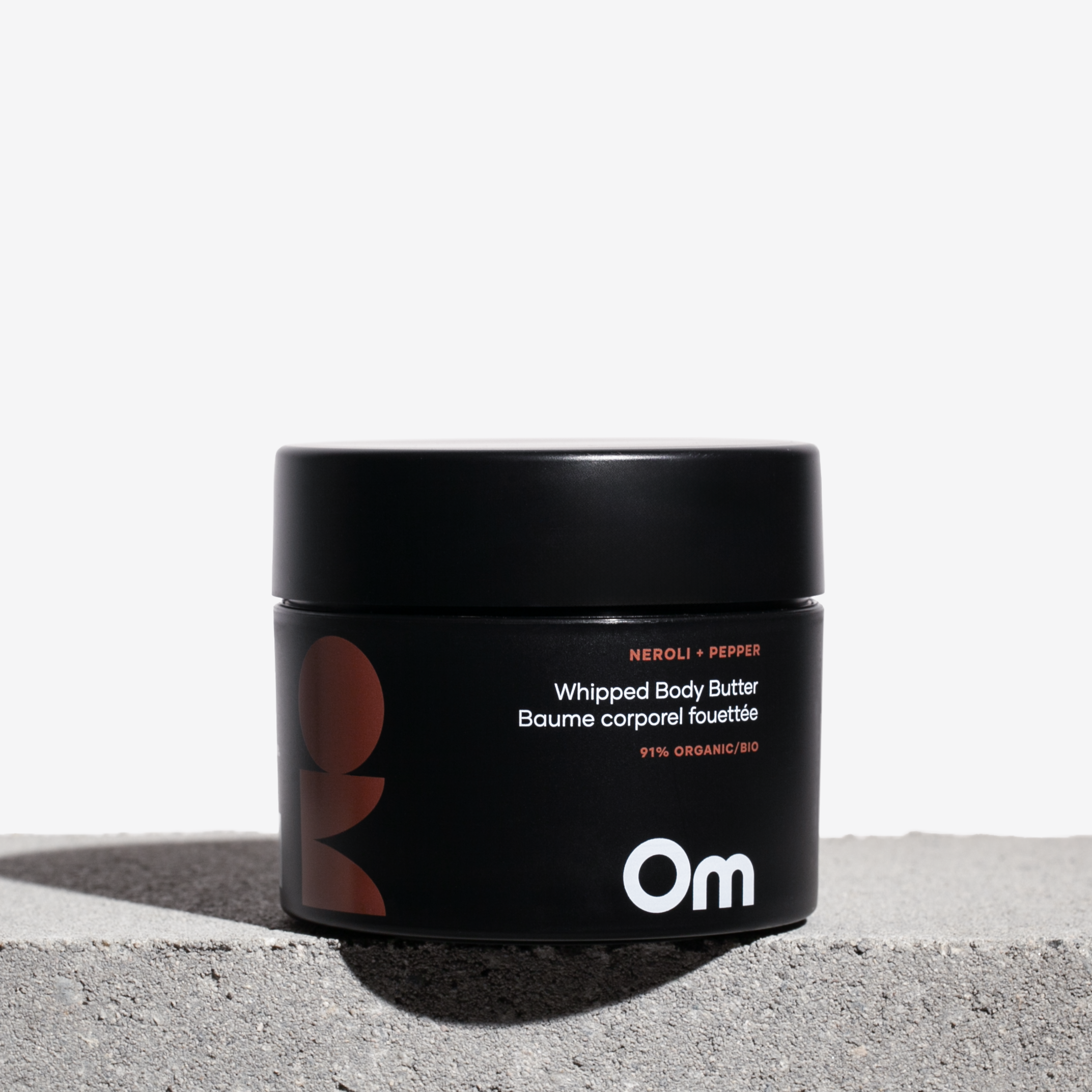 Black jar of Om Organics whipped body butter on a light gray surface with a white background