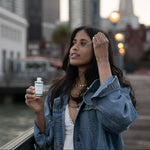 Woman holding a bottle of Graydon Supermoon serum outdoors with blurred cityscape in the background