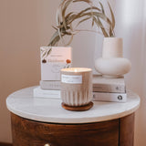 Mimi and August Candle on a marble surface with books and a vase in the background