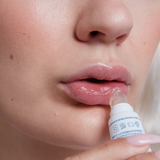 Person applying Three Ships Soft Serve lip balm to their lips with a close-up focus on the action.