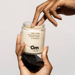 Jar of Om organics body scrub held by a hand with a neutral background
