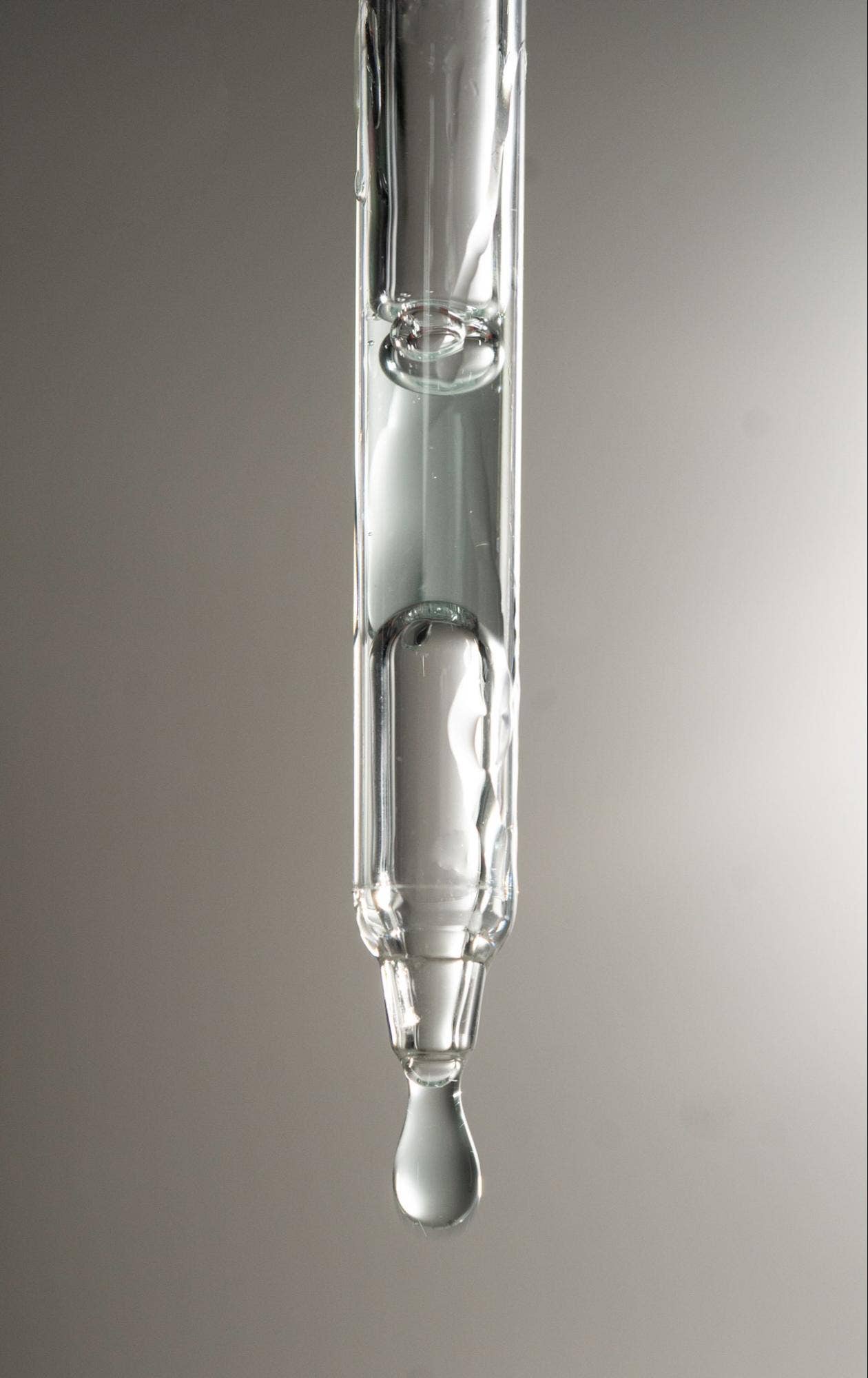 Glass dropper with a drop of Graydon Supermoon serum on a gray background