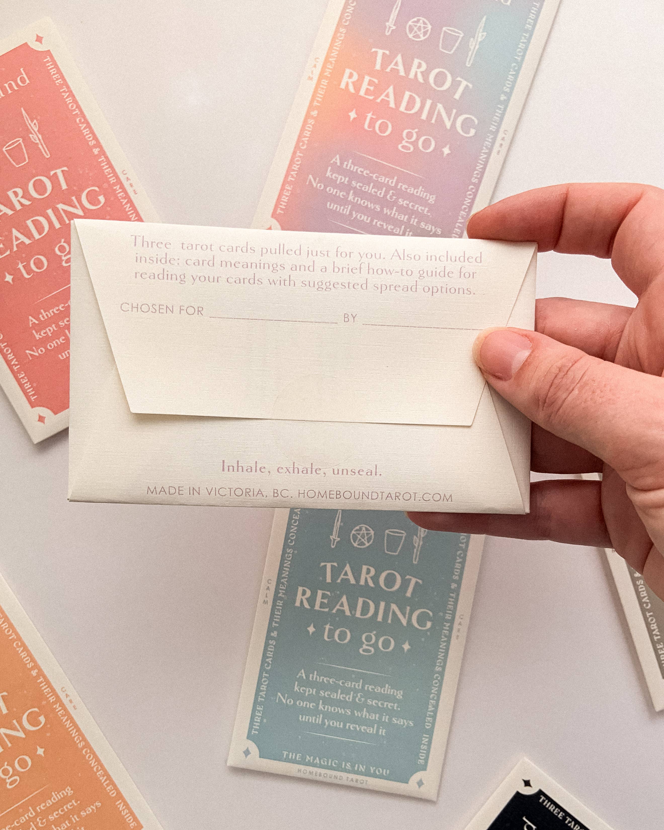 Hand holding a Homebound tarot card envelope with tarot cards in the background