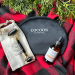 Cocoon Apothecary skincare products on a red and black checkered fabric with greenery.