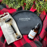 Cocoon Apothecary skincare products on a red and black checkered fabric with greenery.