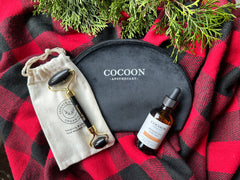 Cocoon Apothecary skincare products on a red and black checkered fabric with greenery.