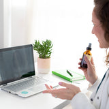 Maria Velve holding a skincare bottle chatting on a laptop on a desk.
