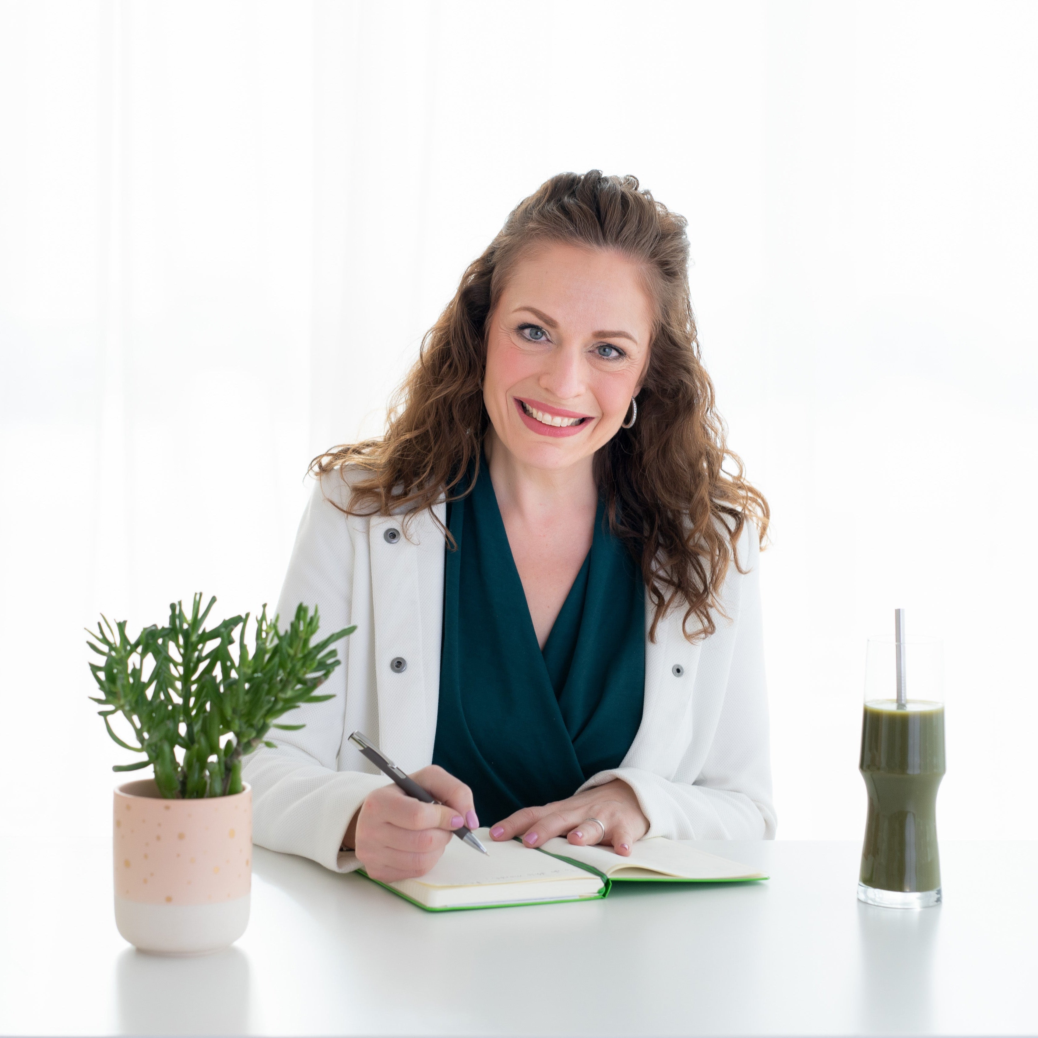 Maria Velve Green Beauty Expert sitting at a desk with a plant and a drink, smiling.