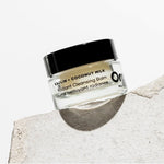 OM Organics Jar of cleansing balm with a black lid on a textured stone surface