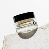 OM Organics Jar of cleansing balm with a black lid on a textured stone surface