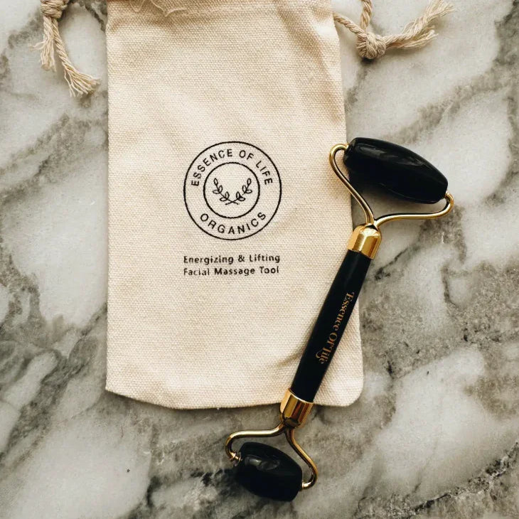 Facial roller with black stones on a marble surface next to a Essence of Life Organics branded pouch.