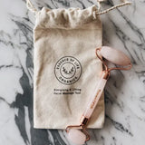 Facial roller with rose gold accents on a beige drawstring bag labeled 'Essence of Life Organics' on a marble surface.