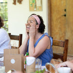 Woman 40+ in blue shirt laughing with a facial mask on. 