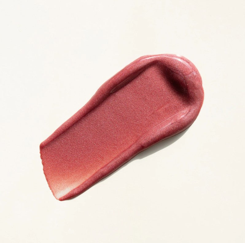 Pink lip shine swatch on a beige background