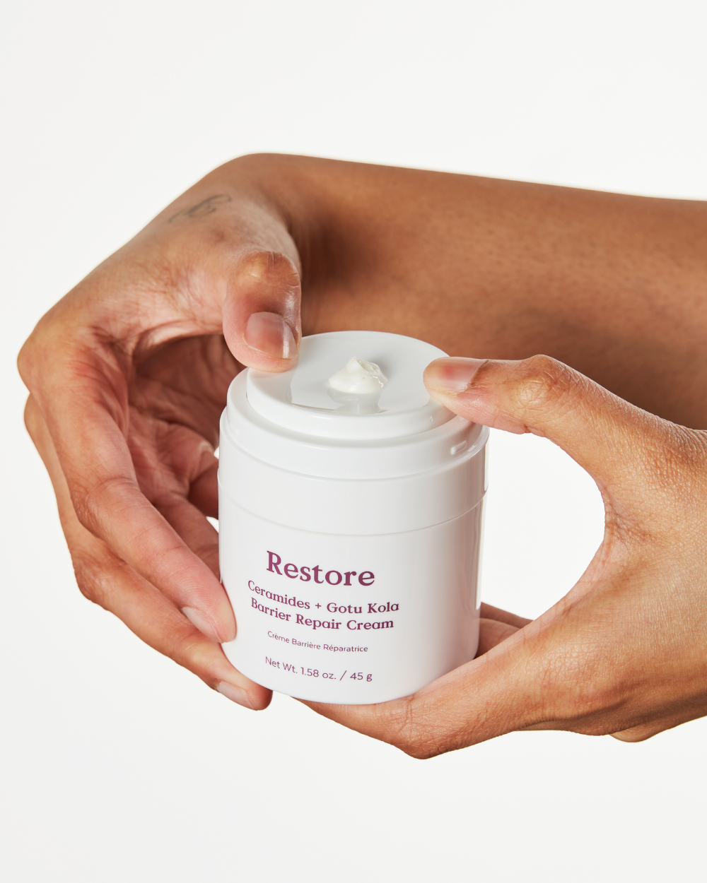 Person holding a jar of Three Ships 'Restore' cream with a white background