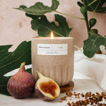 Mimi and August Candle with a label, figs, and leaves on a light background