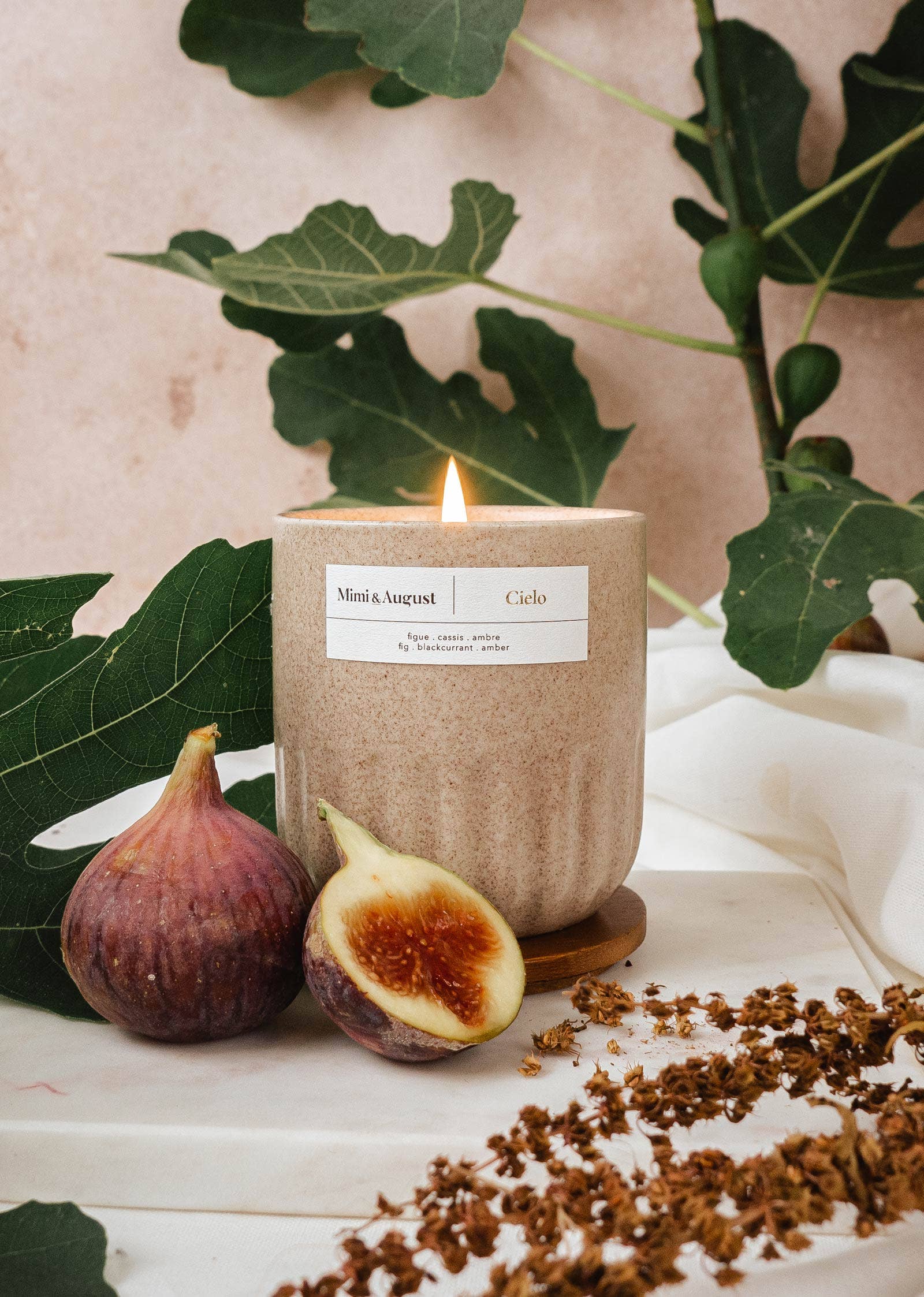 Mimi and August Candle with a label, figs, and leaves on a light background