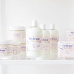 The Bathologist Hydrate skincare products on a white surface with a plant in the foreground