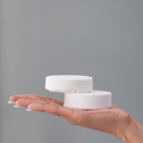 Two white Bathologist shower steamers on a person's palm against a gray background