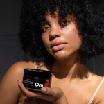 Woman holding a jar of Om Organics body butter against a dark background