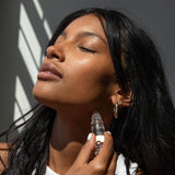 Woman applying Om perfume roll on to her neck with a bottle against a neutral background