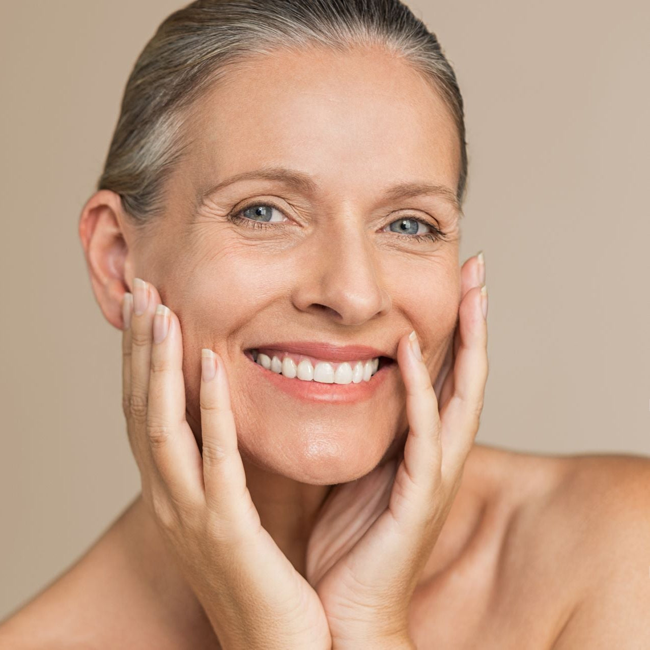 Woman with clear skin touching her face against a beige background