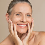 Woman with clear skin touching her face against a beige background